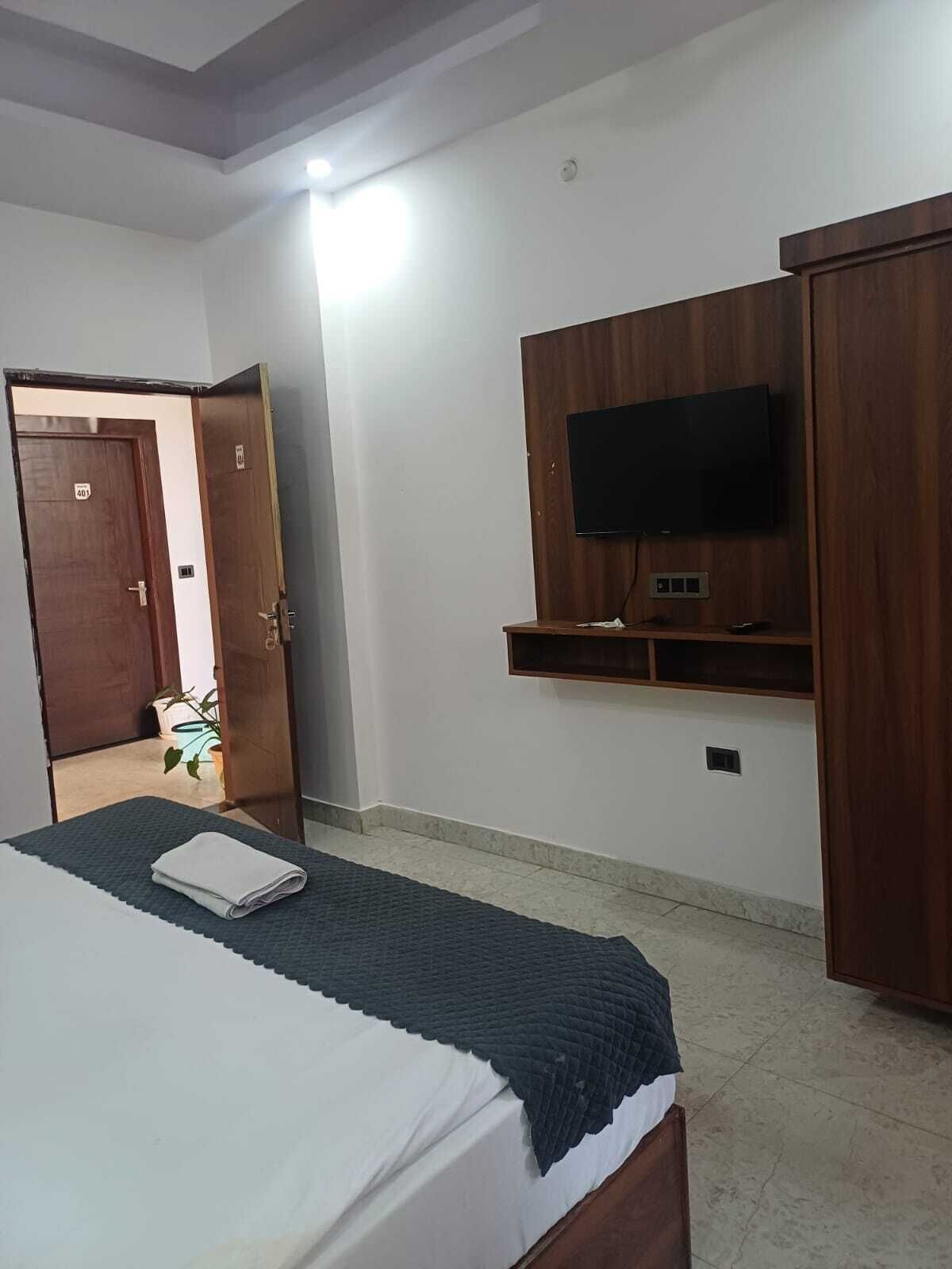 A bedroom with a bed, a TV mounted on a wooden panel, and a door leading to another room.