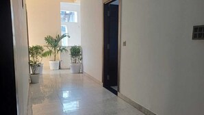A hallway with tiled flooring, potted plants, and a door leading to another room. - The Hotel JRS (Rishikesh)