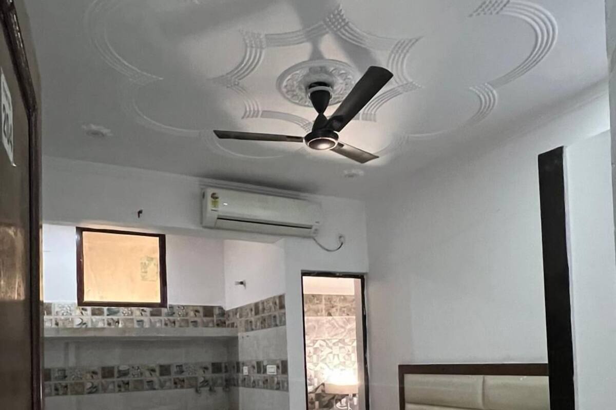 Habitación de hotel con cama, una pequeña zona de estar con un banco, ventilador de techo, aire acondicionado y vistas al exterior a través de una puerta.