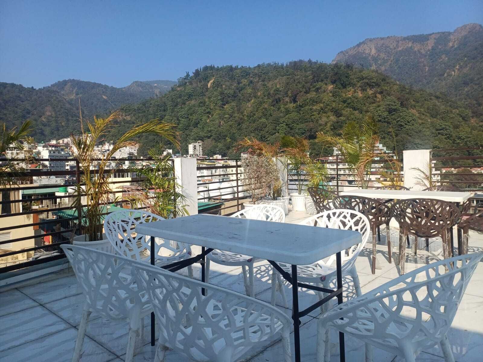 A rooftop terrace with white outdoor furniture, surrounded by city buildings and a mountainous backdrop.