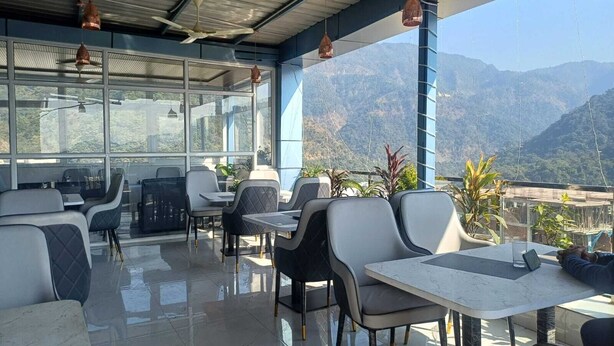 A restaurant with a terrace overlooking mountains, featuring modern furniture and large windows. - The Hotel JRS (Rishikesh)