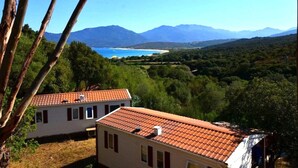 Una casa con techo de tejas rojas y vista a un paisaje costero con montañas al fondo.