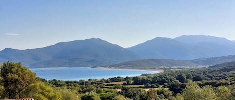 A coastal landscape with mountains in the background, a clear sky, and a view of the sea.