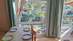 Mesa de comedor dispuesta con platos, vasos y cubiertos, ubicada cerca de una ventana con cortinas que da a un jardín y una terraza.