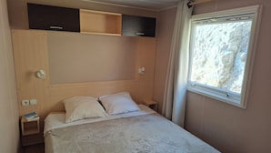 Un dormitorio con cama, mesita de noche, estante empotrado y ventana con cortinas.