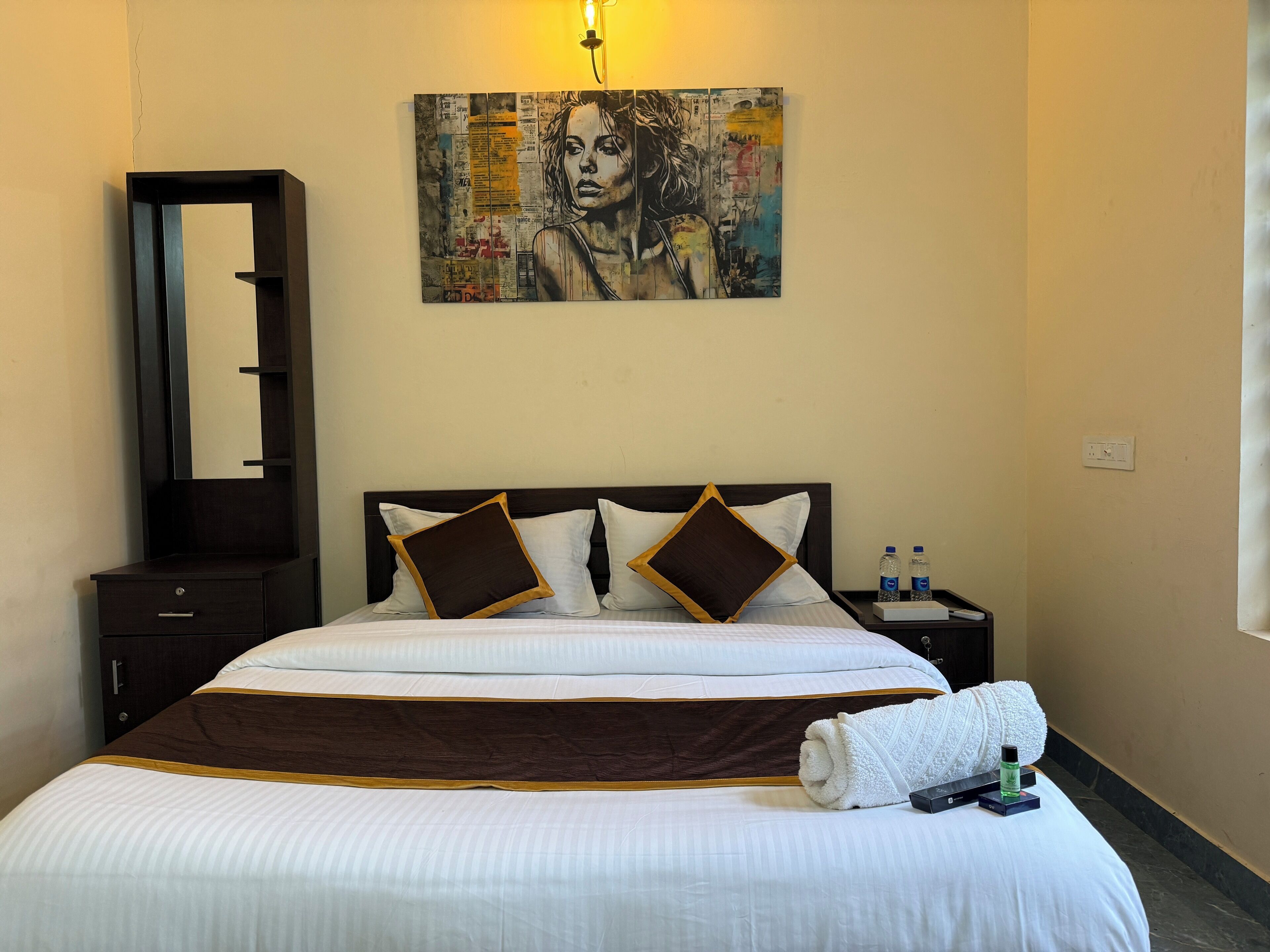 A hotel room with a large bed, a nightstand, a mirror, and a painting on the wall.