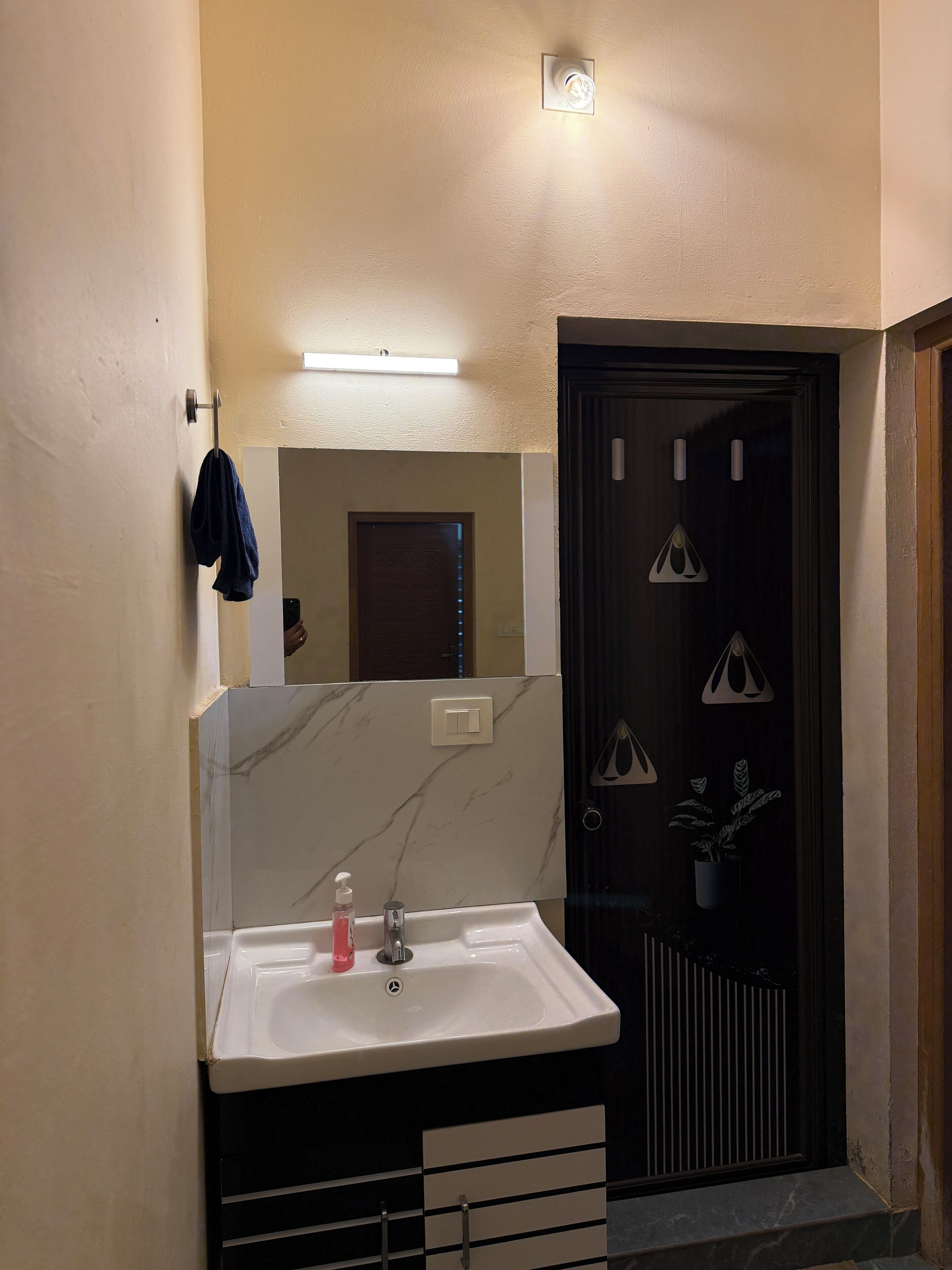 Un baño con un lavamanos blanco, un espejo y una puerta oscura.