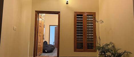 A hallway with a wooden door, a potted plant, and a small step leading to a room.