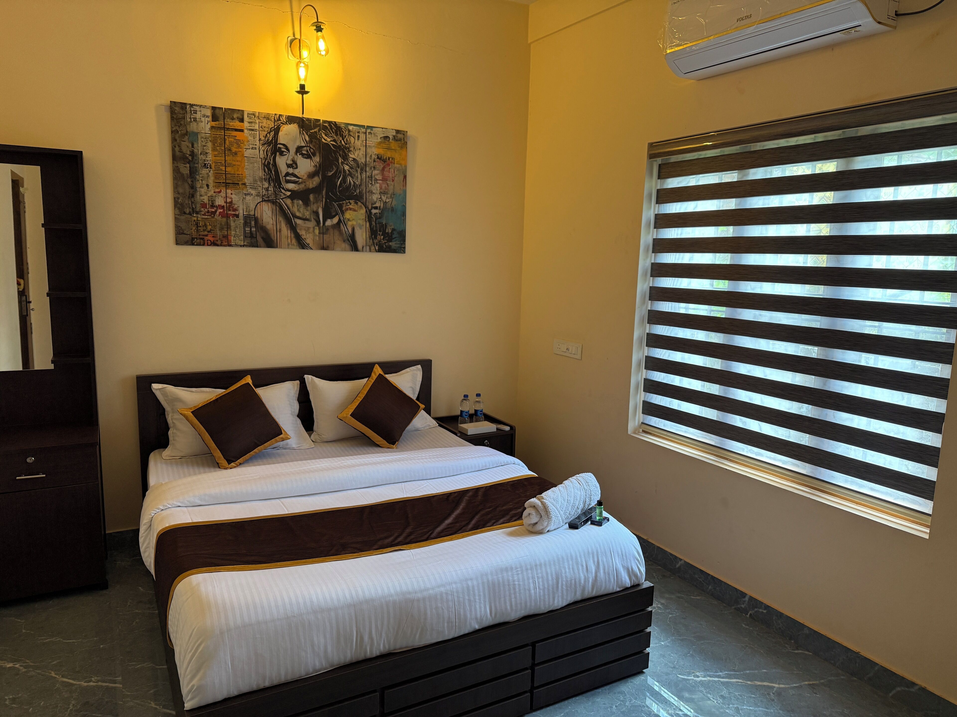 A neatly made bed with white and brown bedding, a dark headboard, and a large wall art piece above it.