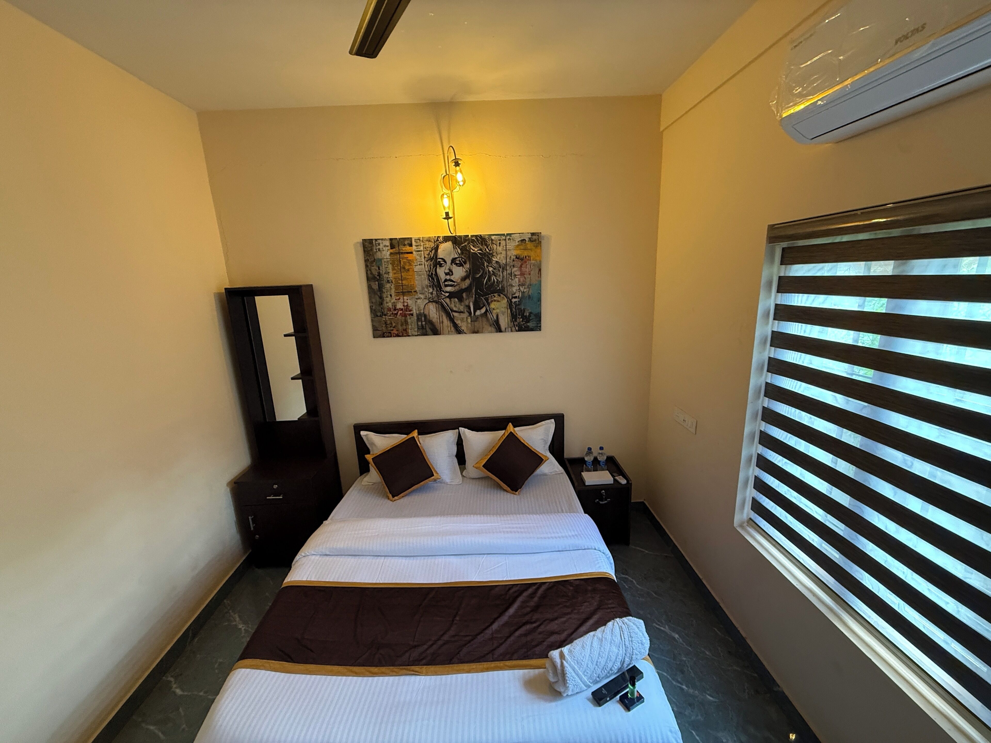 A hotel room with a bed, bedside table, nightstand, and a painting on the wall.
