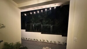 Een buitenruimte met een verhard pad, plantenbakken en een raam met lichtjes.