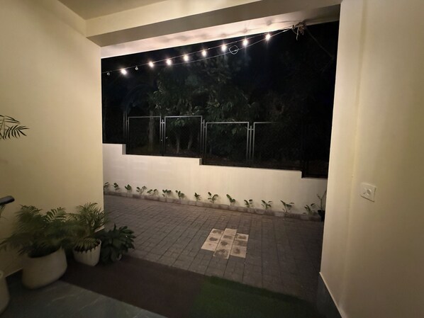An outdoor area with a paved walkway, potted plants, and a window with string lights. - The Family Sport Homestay Wayanad (Sulthan Bathery)