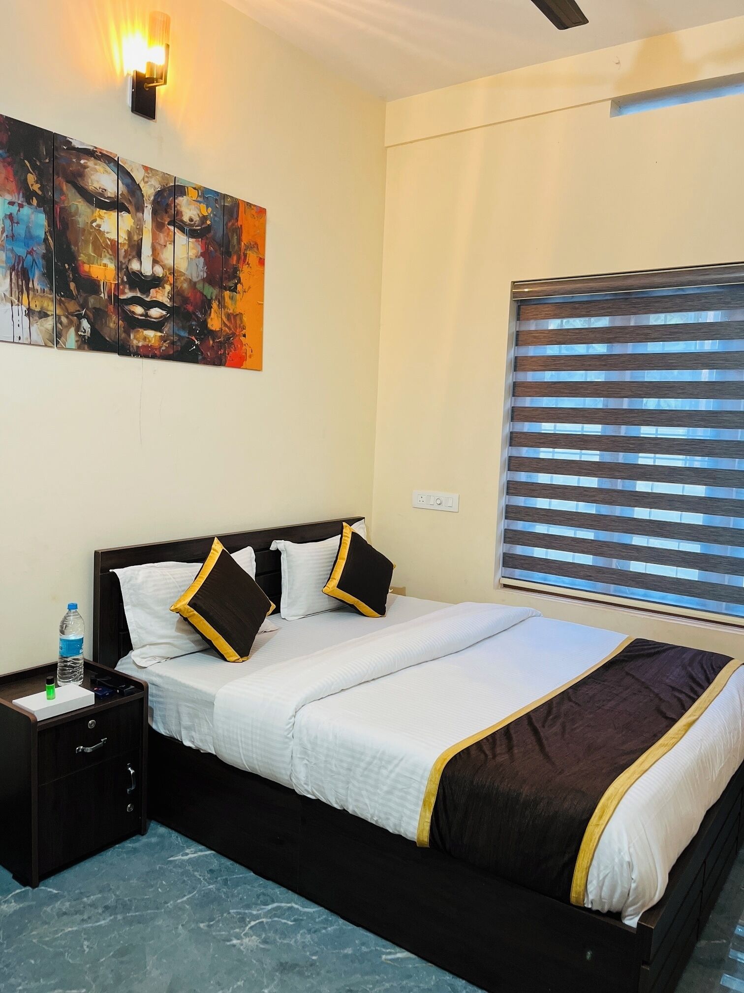 A hotel room with a bed, a nightstand, a water bottle, and a painting on the wall.