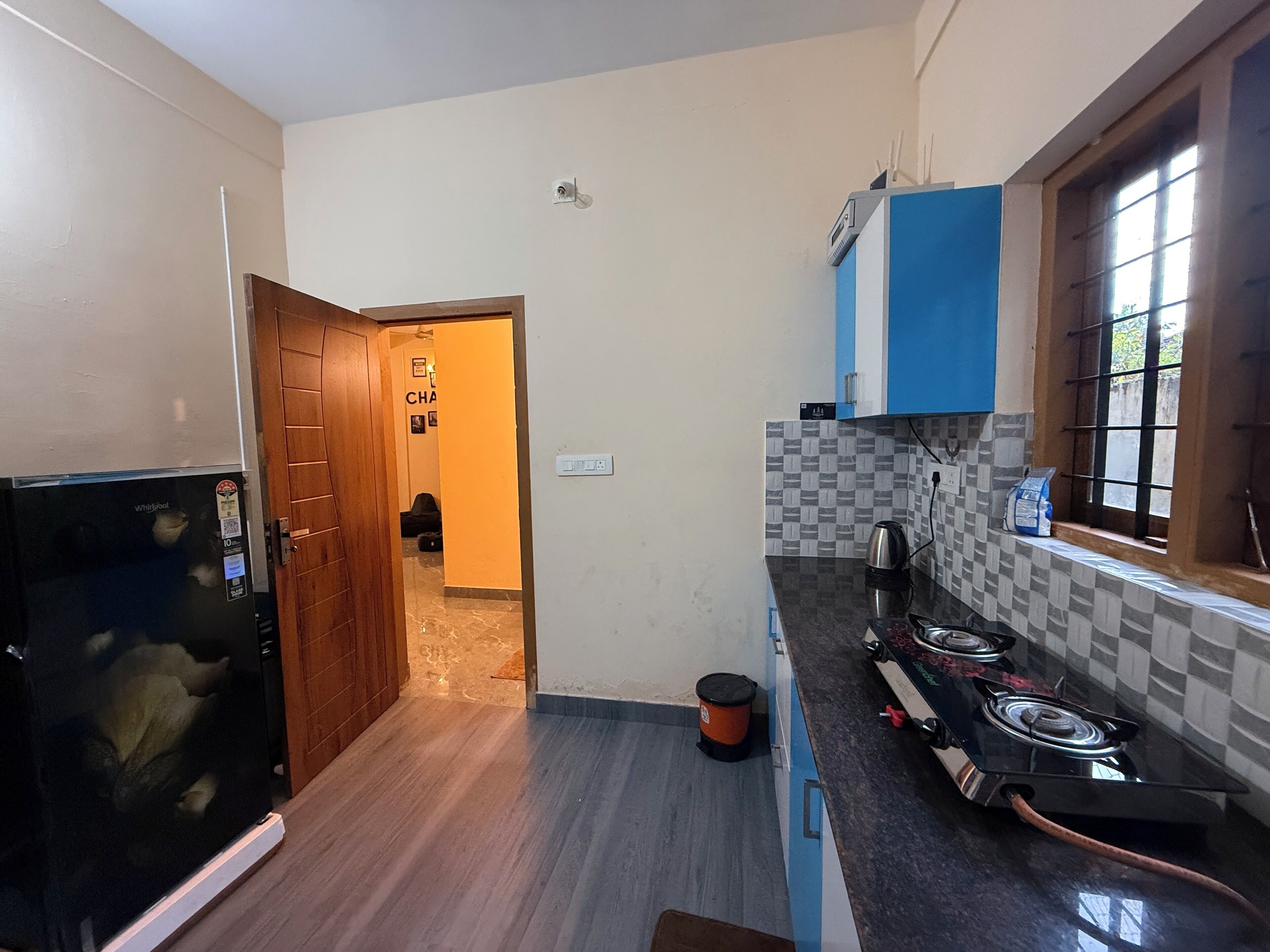 A kitchen with a refrigerator, stove, and a window with bars.