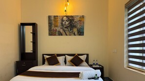 Een hotelkamer met een groot bed, een nachtkastje, een spiegel, een schilderij aan de muur en een raam met jaloezieën.