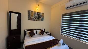 A bedroom with a bed, a nightstand, a mirror, an air conditioner, and a window with blinds.