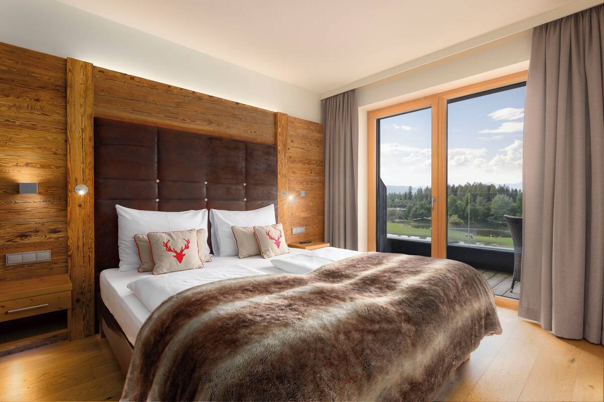 Ein Schlafzimmer mit einem großen Bett, einem Holzkopfstück und Blick auf eine grüne Landschaft durch ein großes Fenster.