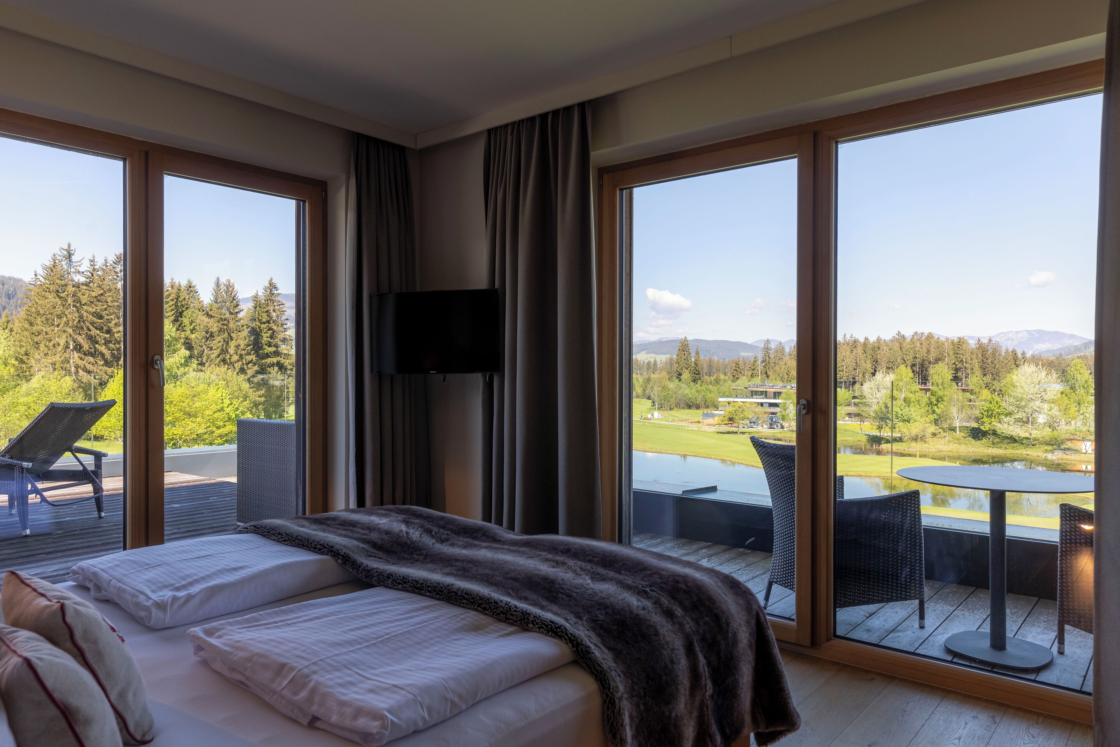 Ein Hotelzimmer mit einem großen Bett, einem Fernseher und einem Balkon mit Blick auf einen Golfplatz und Berge.