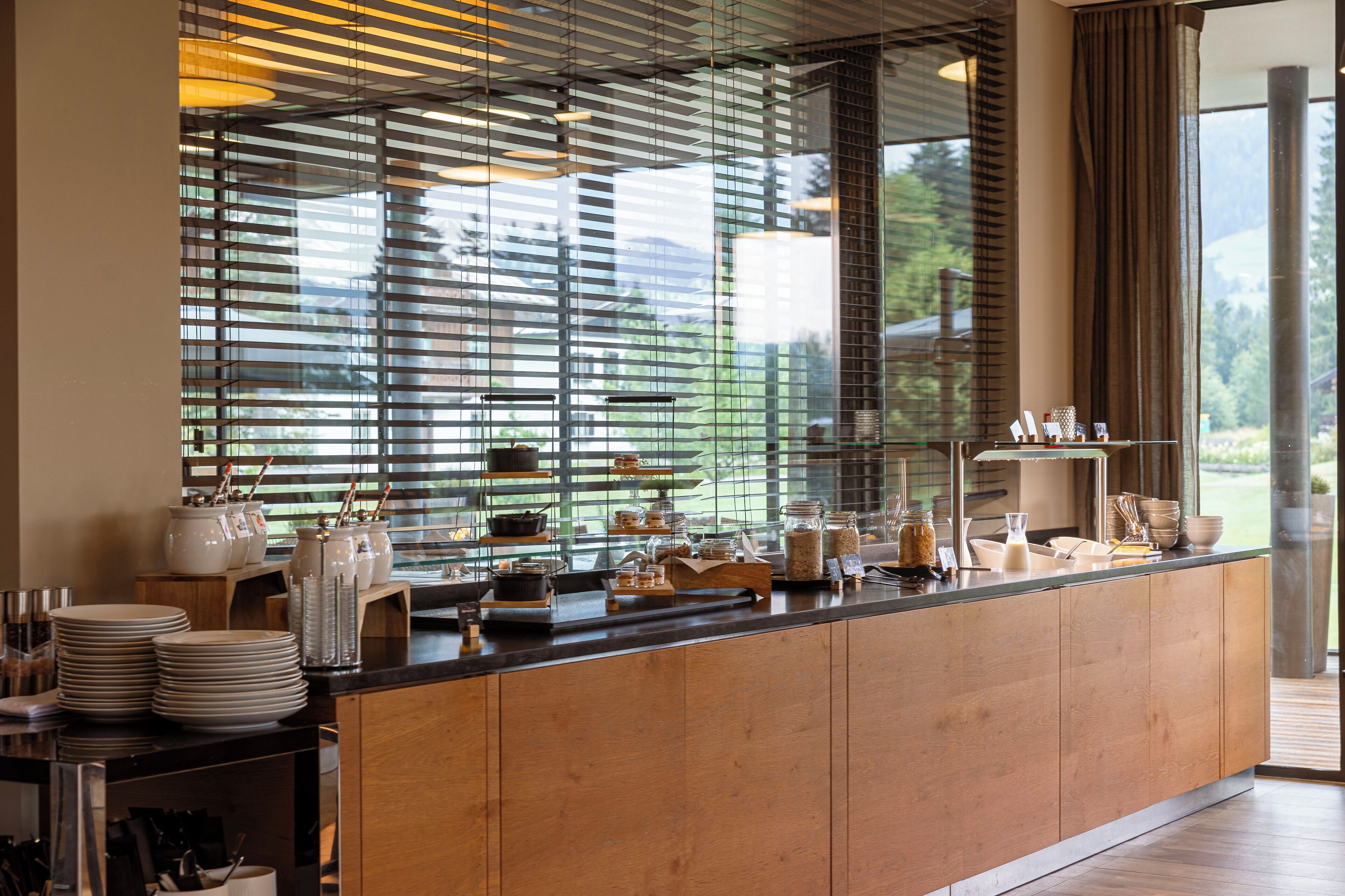 A modern kitchen with a wooden countertop, glass display case, and a view of the outdoors through large windows.