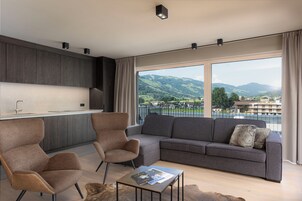 Una sala de estar moderna con un sofá, dos sillones, una mesa de centro y vistas a un paisaje montañoso a través de amplios ventanales.