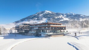 A modern building with a glass facade, surrounded by snow-covered landscape and a mountain in the background. - Berg & Golf Apartments Westendorf by ALPS RESORTS (Westendorf)