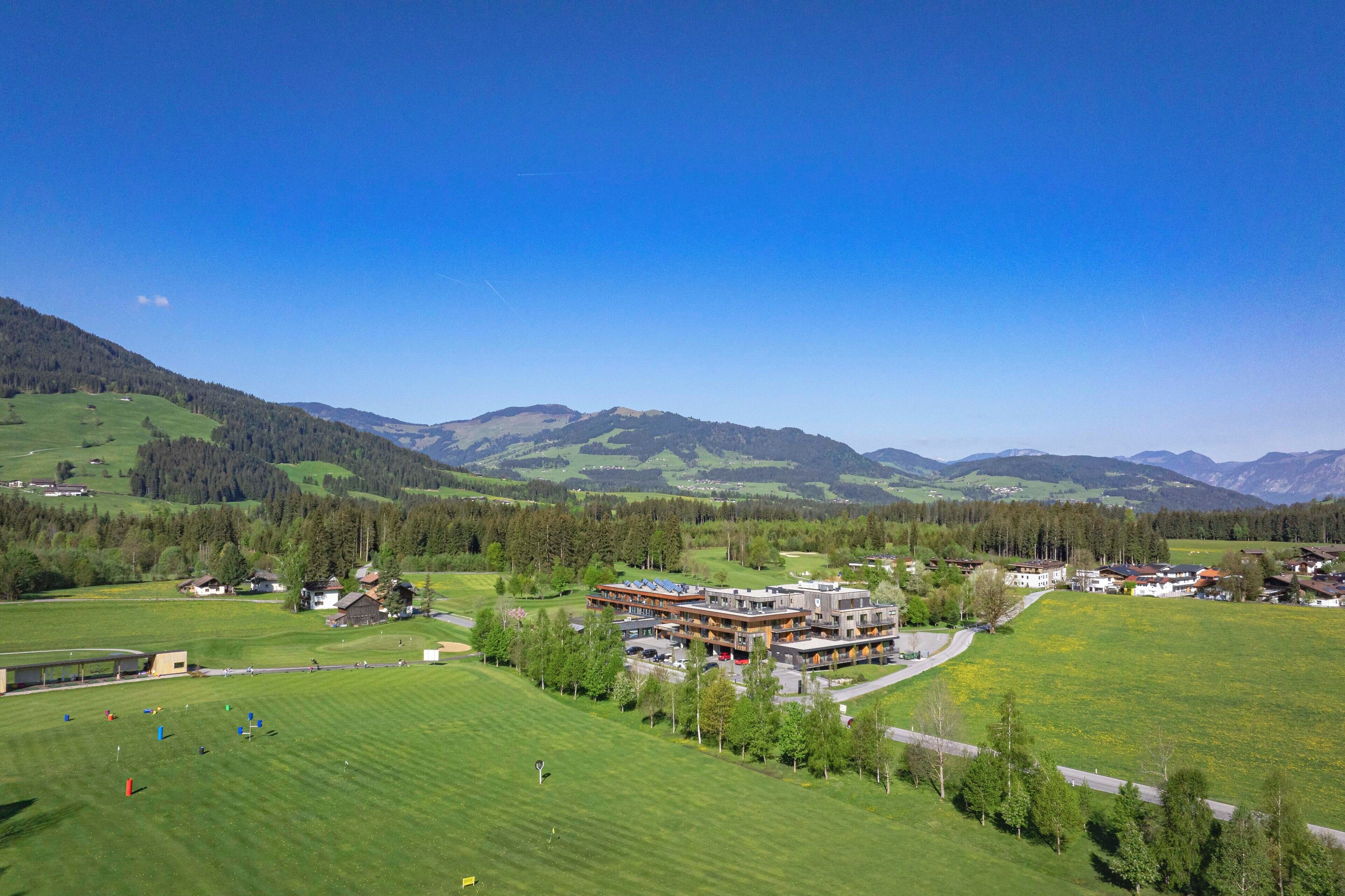 A hotel with multiple buildings, surrounded by green fields and mountains.
