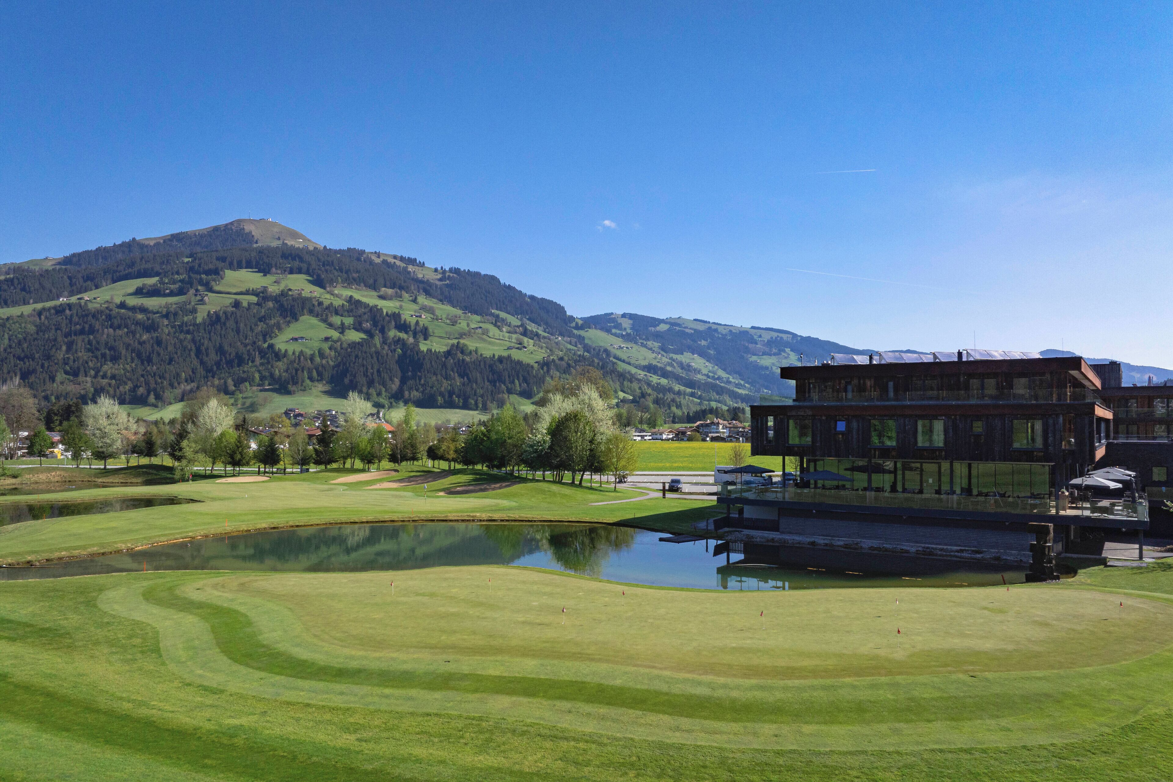 A golf course with a pond, a wooden building, and a mountain in the background.