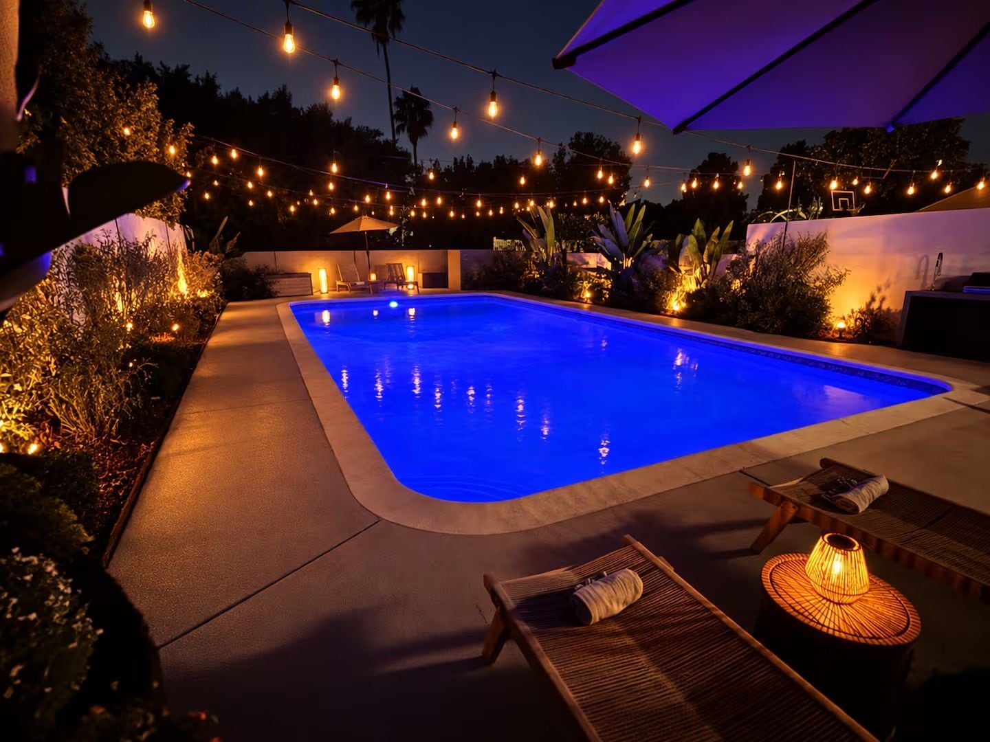 A swimming pool with a blue tint, surrounded by outdoor furniture and string lights.