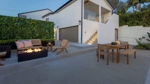 Et moderne hus med bålsted, udendørs siddepladser og trappe op til en balkon.