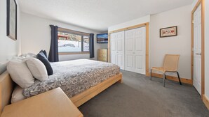A bedroom with a bed, a chair, a wardrobe, and a window with a view of a snowy street. - Nestle Inn Hideaway - Toby Creek Lodge Unit 213 (Area F (Columbia Lake/Windermere Lake))