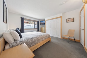 A bedroom with a bed, a chair, a wardrobe, and a window with a view of a snowy street. - Nestle Inn Hideaway - Toby Creek Lodge Unit 213 (Area F (Columbia Lake/Windermere Lake))