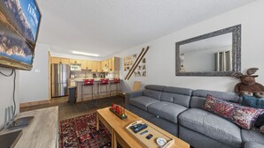 A modern living room with a grey sofa, a wooden coffee table, and a TV mounted on the wall. - Nestle Inn Hideaway - Toby Creek Lodge Unit 213 (Area F (Columbia Lake/Windermere Lake))