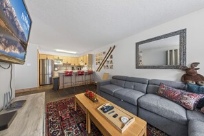 A modern living room with a grey sofa, a wooden coffee table, and a TV mounted on the wall. - Nestle Inn Hideaway - Toby Creek Lodge Unit 213 (Area F (Columbia Lake/Windermere Lake))