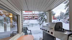 A covered outdoor area with a grill, a table, and a view of a snowy landscape. - Nestle Inn Hideaway - Toby Creek Lodge Unit 213 (Area F (Columbia Lake/Windermere Lake))