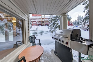 A covered outdoor area with a grill, a table, and a view of a snowy landscape. - Nestle Inn Hideaway - Toby Creek Lodge Unit 213 (Area F (Columbia Lake/Windermere Lake))