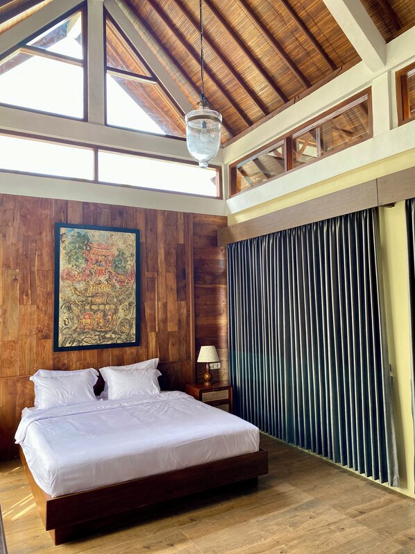 Un dormitorio amplio con una cama grande, paredes de madera, un ventilador de techo y un ventanal.