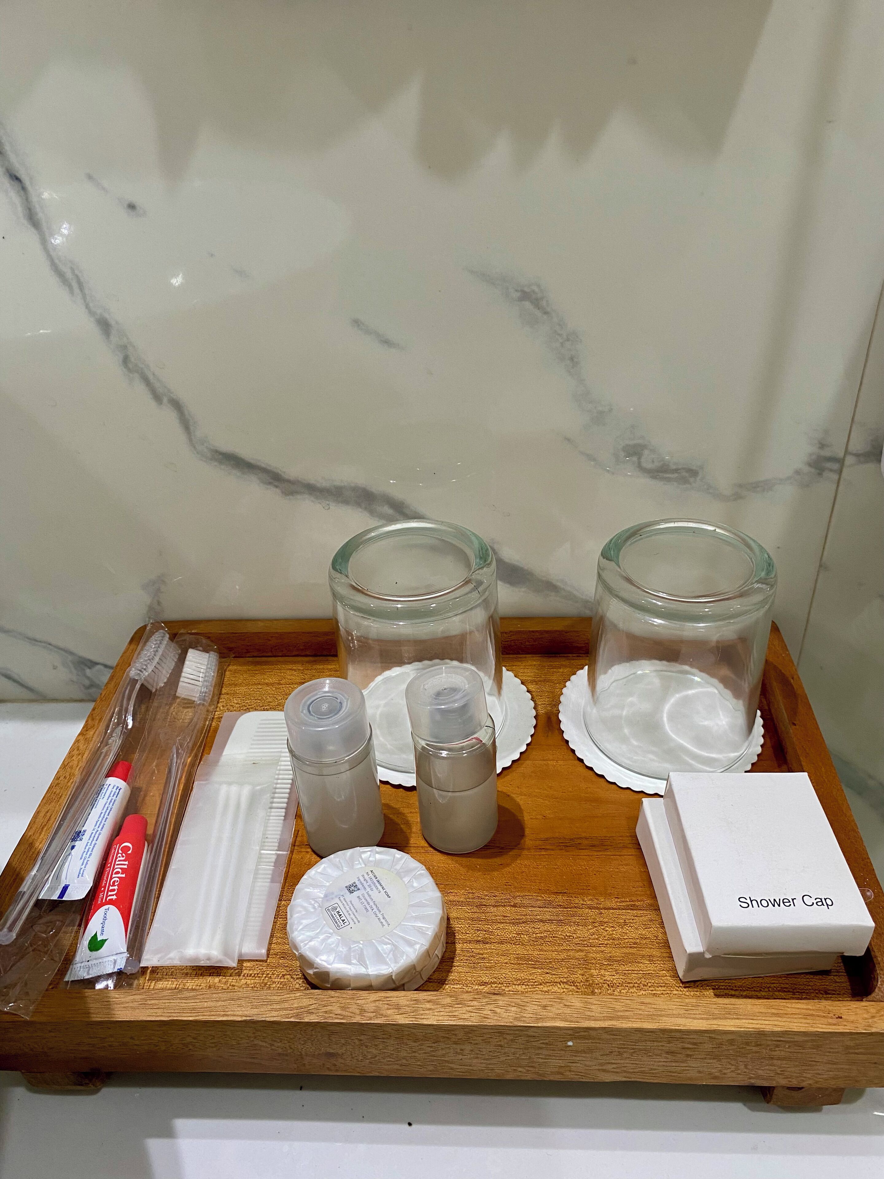 A wooden tray with toiletries including a toothbrush, toothpaste, a shower cap, and two glass containers.