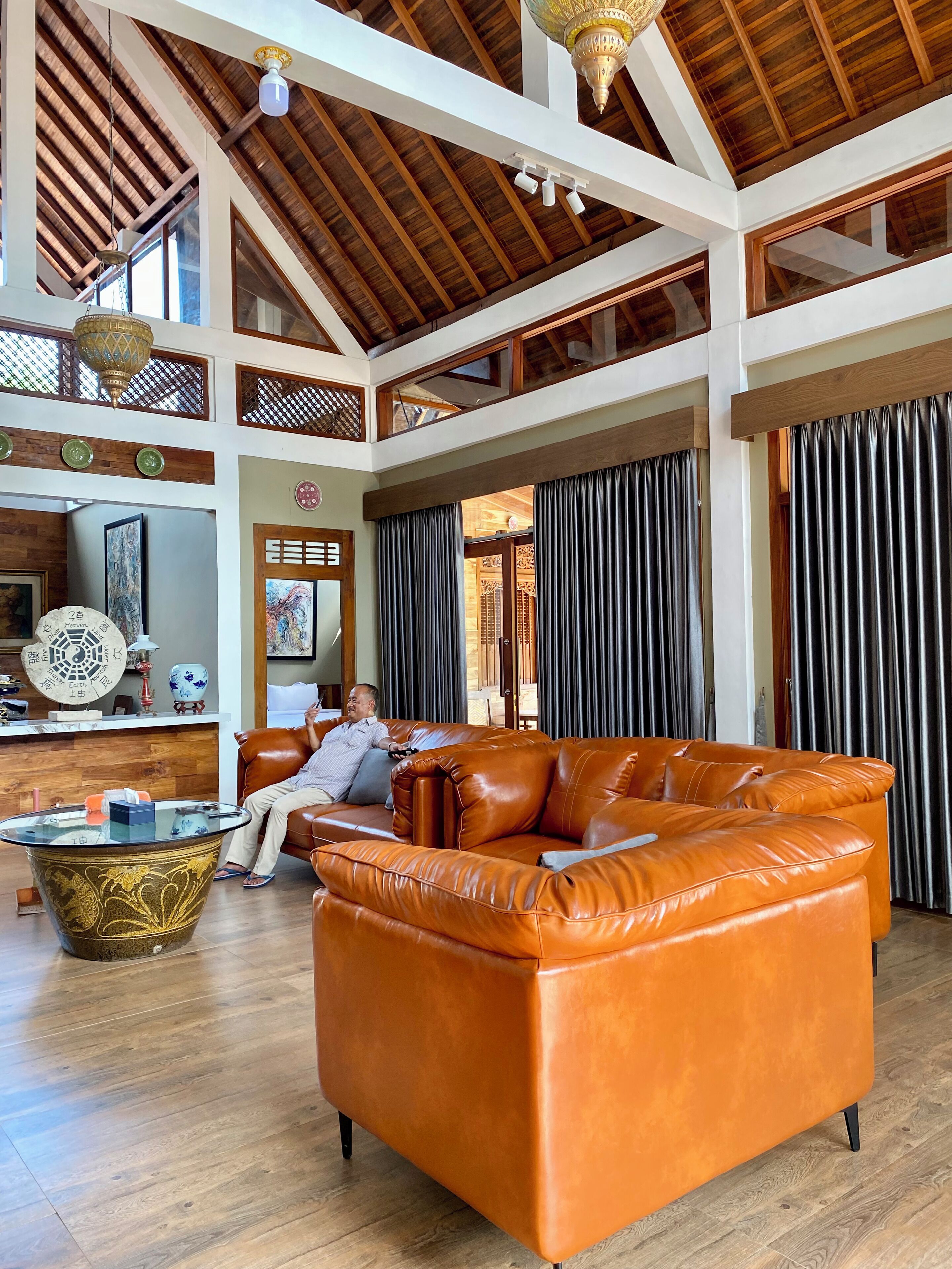 A spacious living area with a large orange leather sofa, a glass coffee table, and a wooden ceiling with exposed beams.
