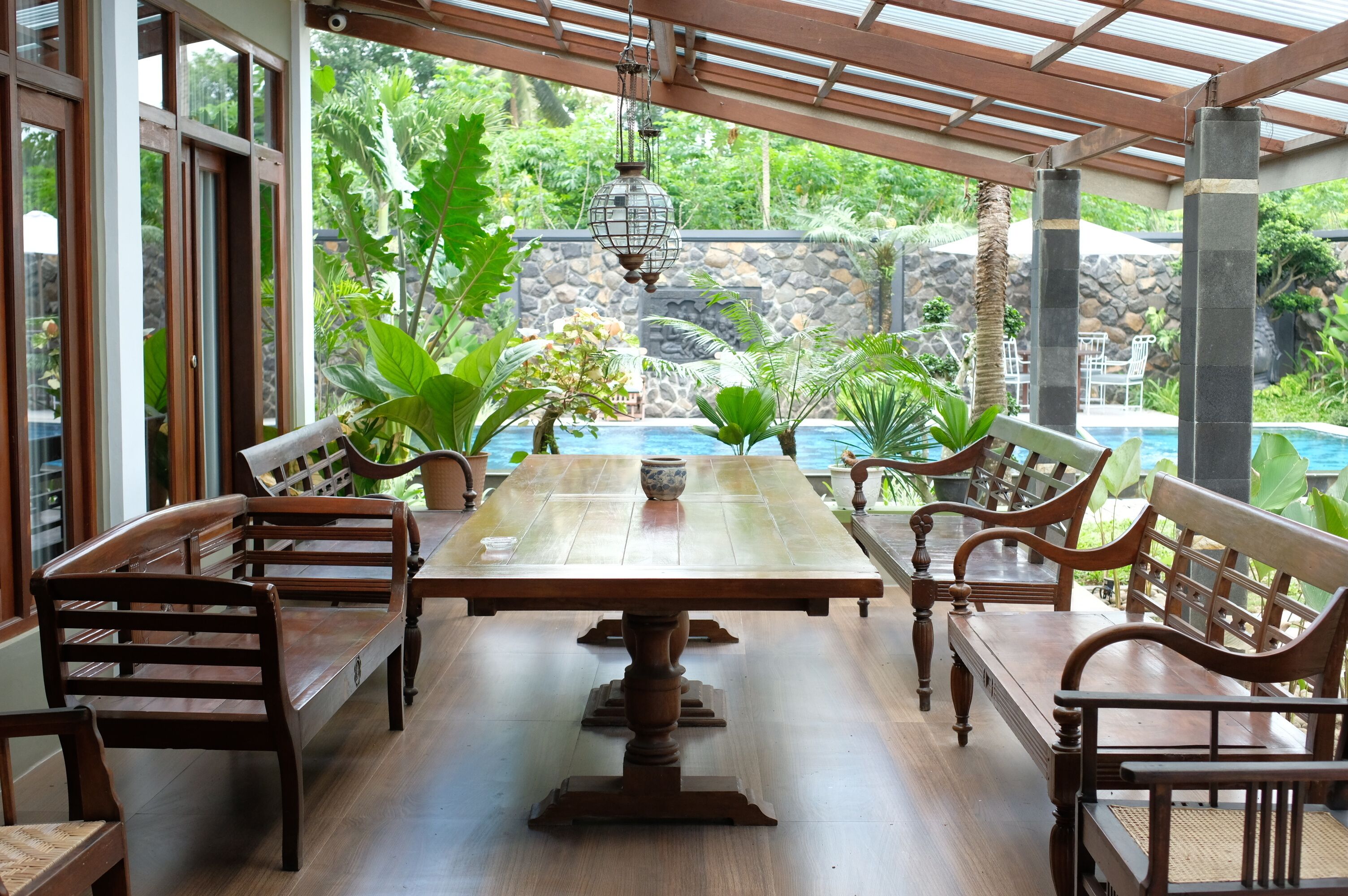 Une table à manger en bois, avec des bancs, entourée de plantes en pot et offrant une vue sur une piscine.