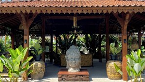 Ein traditioneller Pavillon mit Ziegeldach, einer zentralen Buddha-Statue und umliegenden Topfpflanzen.