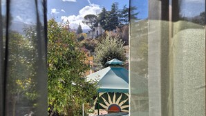 Blick durch ein Fenster mit einem Metallgeländer, einer Steinmauer und einem grünen Sonnenschirm.
