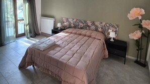 Ein Schlafzimmer mit einem großen Bett, einem Nachttisch, einer Lampe, einem Heizkörper und einem Fenster mit Vorhängen.