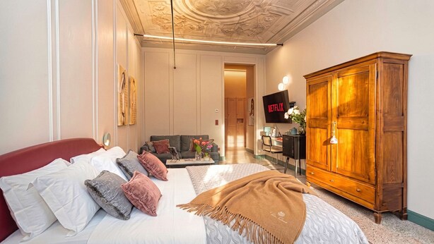 Una camera d'albergo con un letto, un divano, un armadio in legno, una televisione e una scrivania con una sedia.