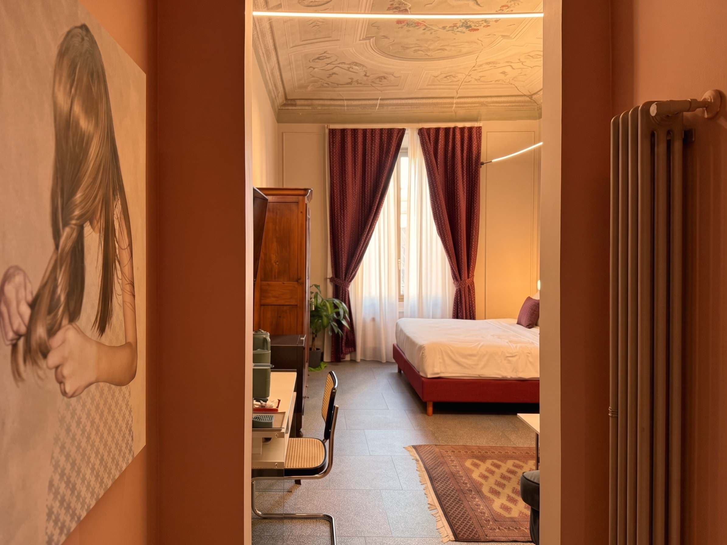Une chambre d’hôtel avec un lit, un bureau avec une chaise, un radiateur et une fenêtre avec des rideaux.
