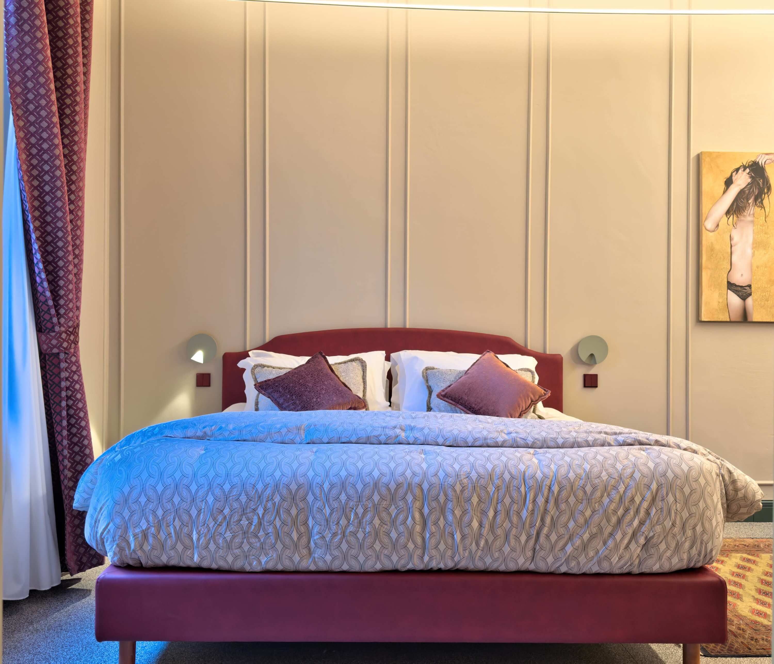 Une chambre d’hôtel avec un lit, une tête de lit, une lampe fixée au mur et un tableau.
