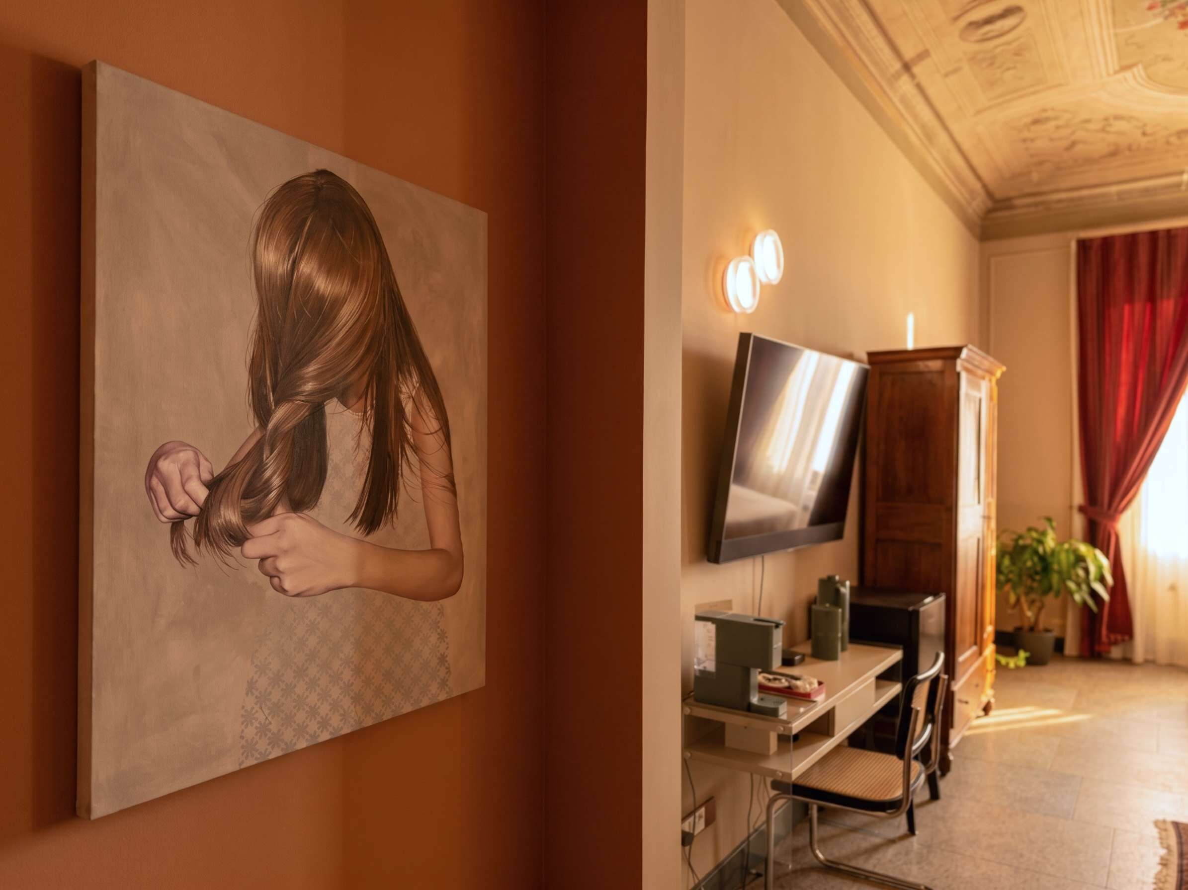 Une pièce comprenant un tableau représentant une personne, un téléviseur à écran plat, un bureau avec un ordinateur et une plante en pot.