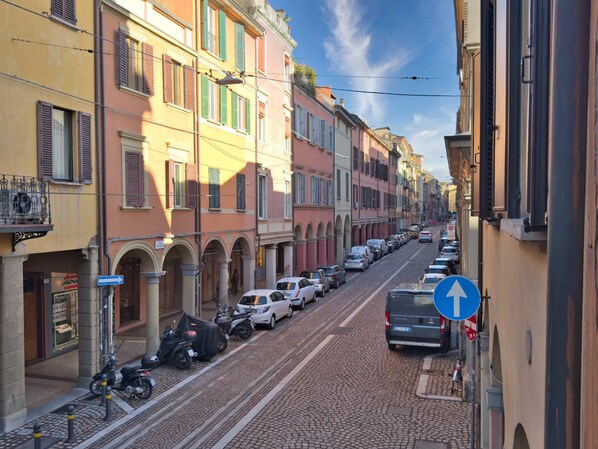 Eine Kopfsteinpflasterstraße gesäumt von bunten Gebäuden, parkenden Autos und einem klaren, blauen Himmel.