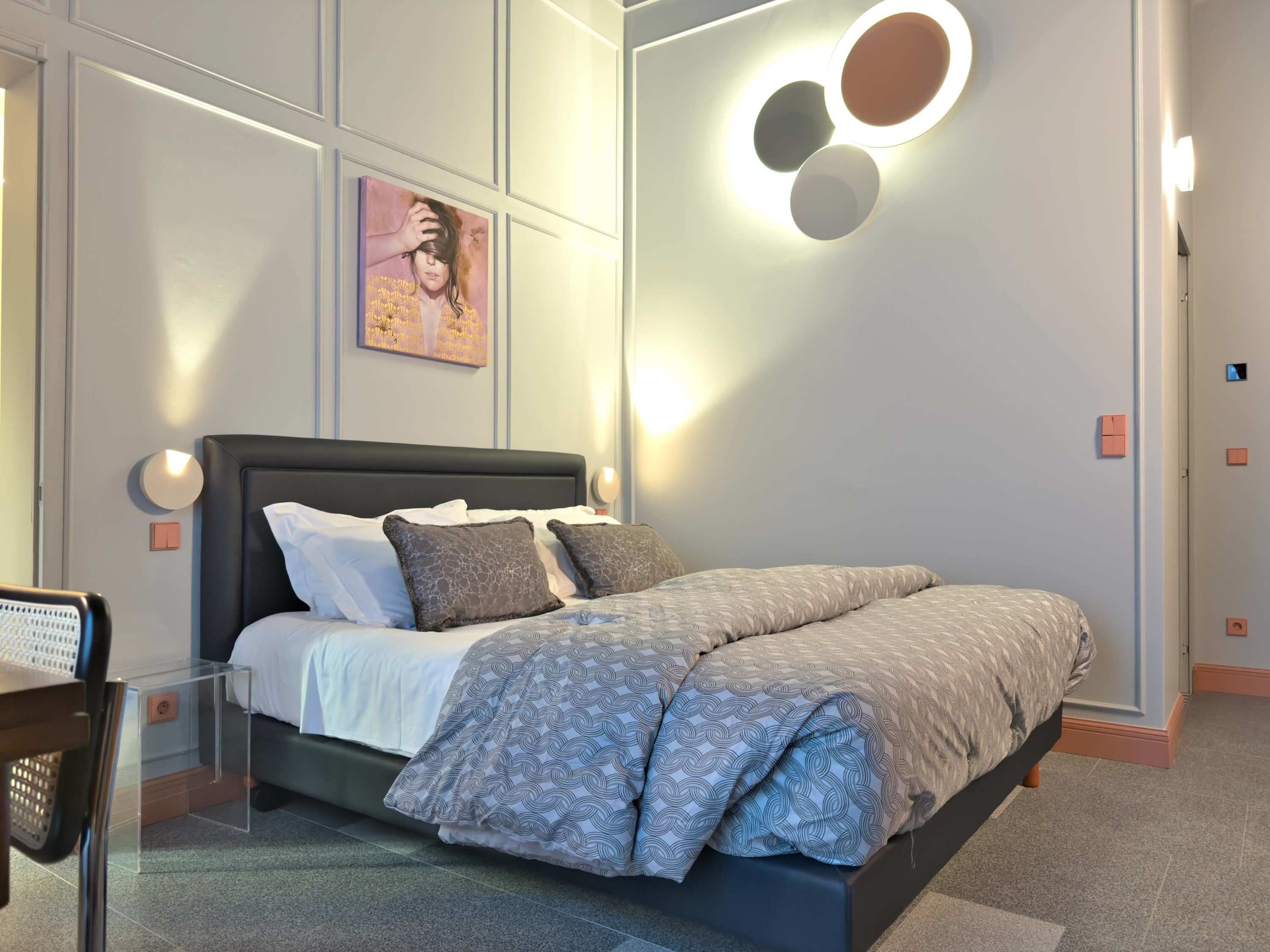 Une chambre moderne avec un lit, des luminaires fixés au mur et un tableau.
