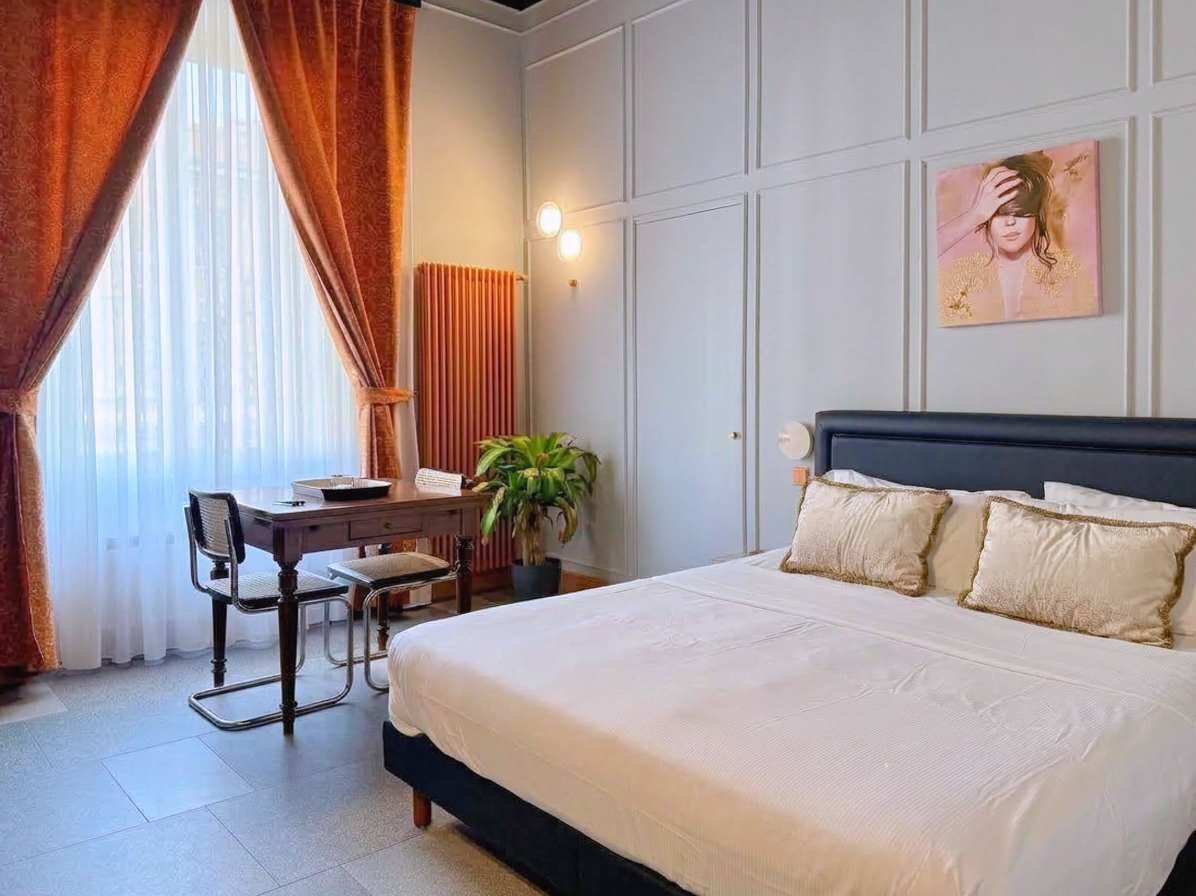 Une chambre d’hôtel avec un lit, un bureau, une chaise, une plante en pot et un tableau au mur.