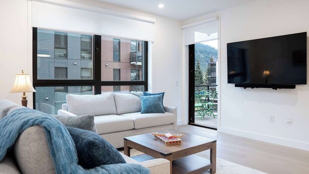 A modern living room with a sofa, coffee table, and a TV mounted on the wall. - Revelstoke - Bluebird- New condo! (Revelstoke)